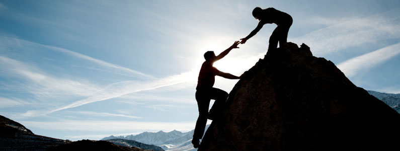 Un uomo tende la mano ad un altro uomo per aiutarlo a salire sopra una roccia