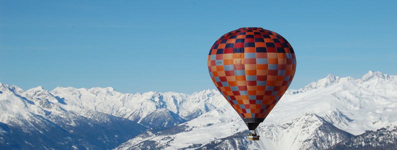 vista di una mongolfiera che sorvola delle montagne innevate