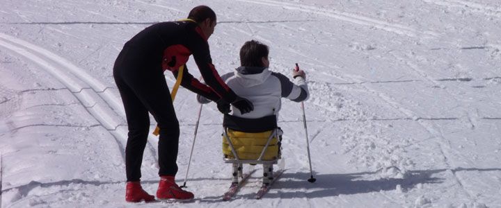 istruttore affianca uno sciatore con disabilità motoria che percorre una pista da sci di fondo