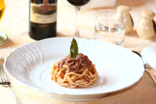 Piatto di spaghetti al ragù serviti a mò di tortino guarnito con una fogliolina d'alloro 