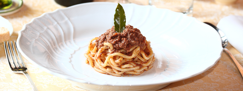 Piatto di spaghetti al ragù serviti a mò di tortino guarnito con una fogliolina d'alloro 