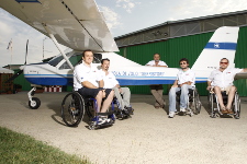 Quattro ragazzi in sedia a rotelle sono in posa con il loro istruttore di volo a fianco dell'aereo ultraleggero della scuola