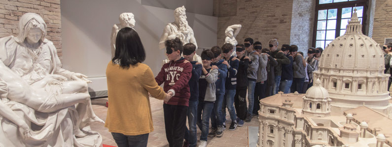 Gruppo di giovani visitatori bendati vengano accompagnati per mano lungo il percorso tattile