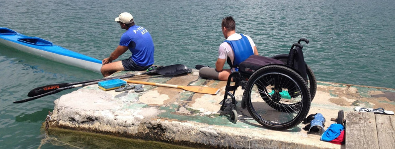 Carrozzina lasciata al molo mentre due sportivi sono in procinto di salire in canoa