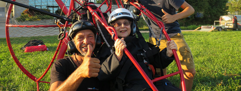 Il pilota e un'anziana signora salutano la fotocamera prima di elevarsi con il parapendio