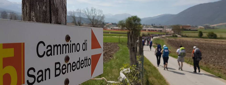 Un cartello che indica San benedetto e sullo sfondo un gruppo di persone sul cammino