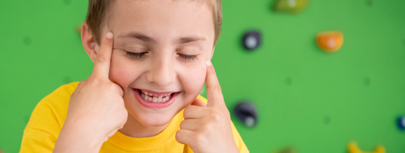 Un bambino sorride ad occhi chiusi e sullo sfondo c'è la parete da arrampicata