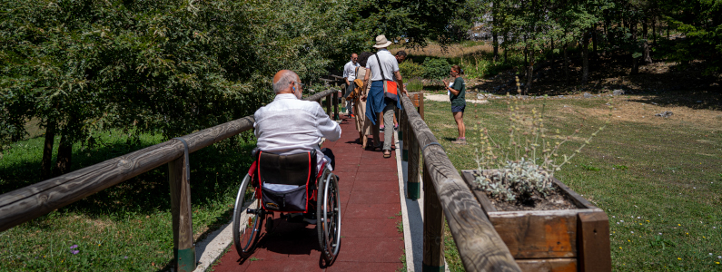 Persona con disabilità in sedia a rotelle percorre il sentiero attrezzato ed ascolta l’audioguida utile alla descrizione della stazione